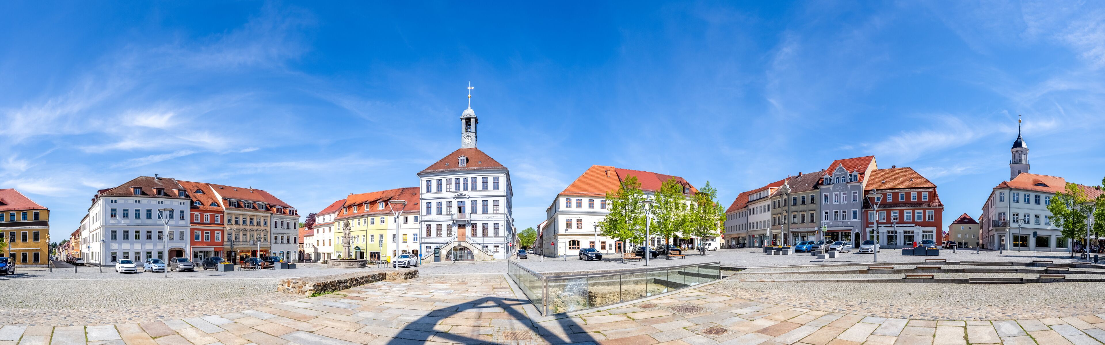 A cobblestone square with historic buildings, a clock tower, and a fountain.