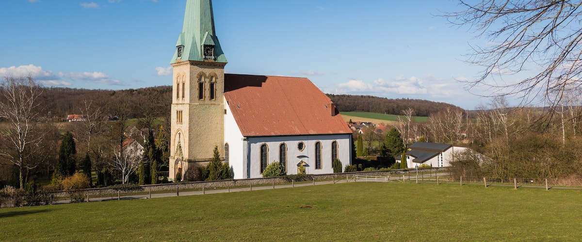 A church with a tall steeple and a red roof, surrounded by a green field and trees.