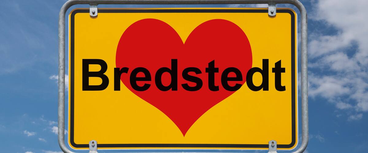 A sign with a heart and the word "Bredstedt" against a blue sky with clouds.