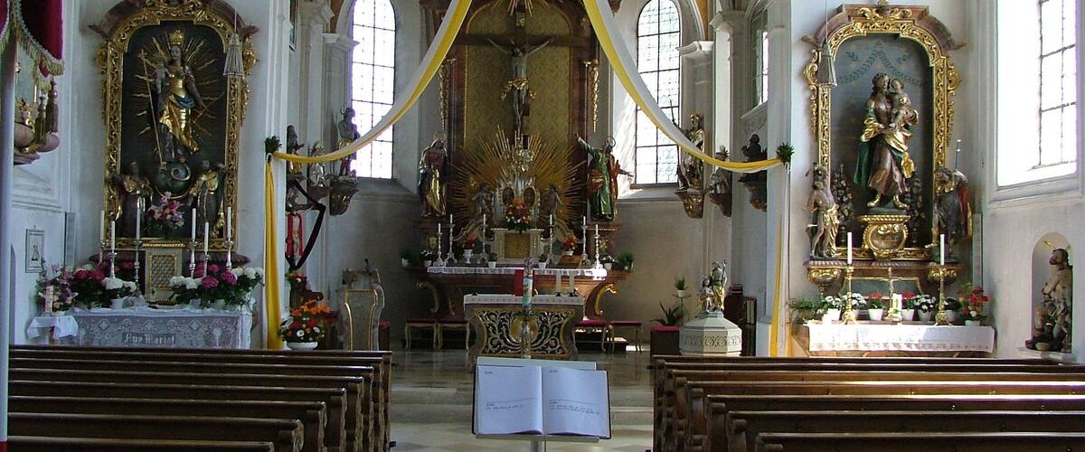 An ornate church interior with high ceilings, golden decorations, and religious statues.