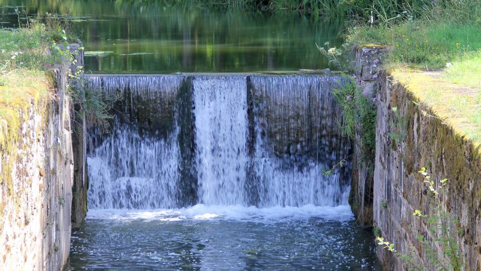 A waterfall cascading into a narrow water channel surrounded by lush greenery.