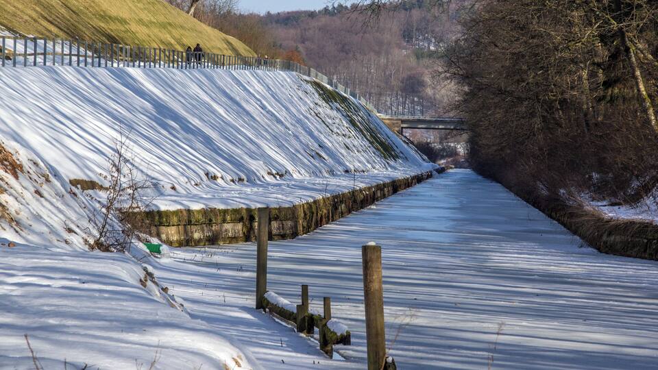 A snow-covered pathway with a wooden fence and a stone wall.