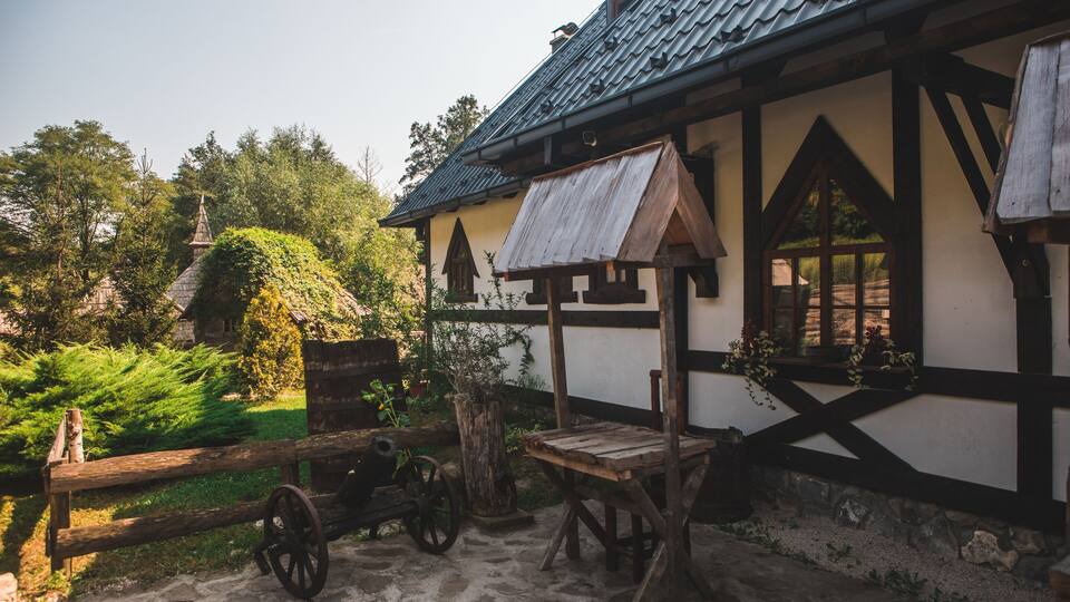 A traditional wooden house with a thatched roof, surrounded by greenery and a stone pathway.