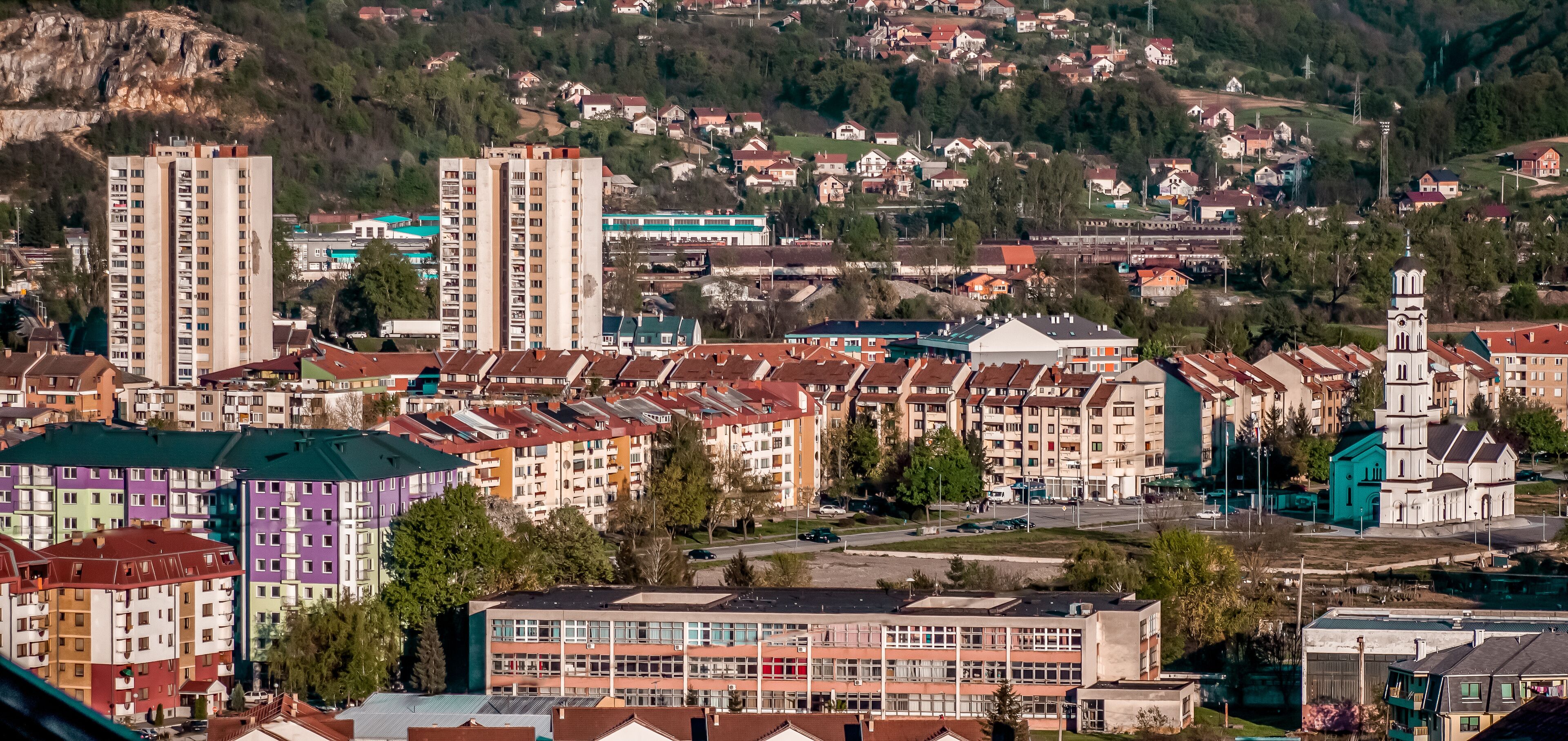 A town with colorful buildings, a church with a tower, and a hill in the background.