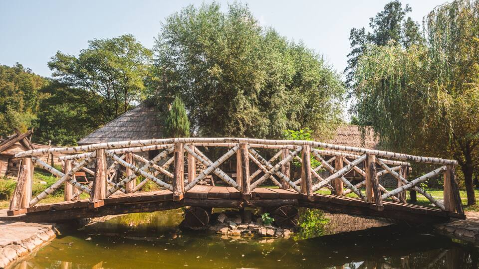 A wooden bridge over a pond with trees in the background.