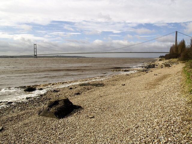 A pebbly beach with a bridge in the distance.
