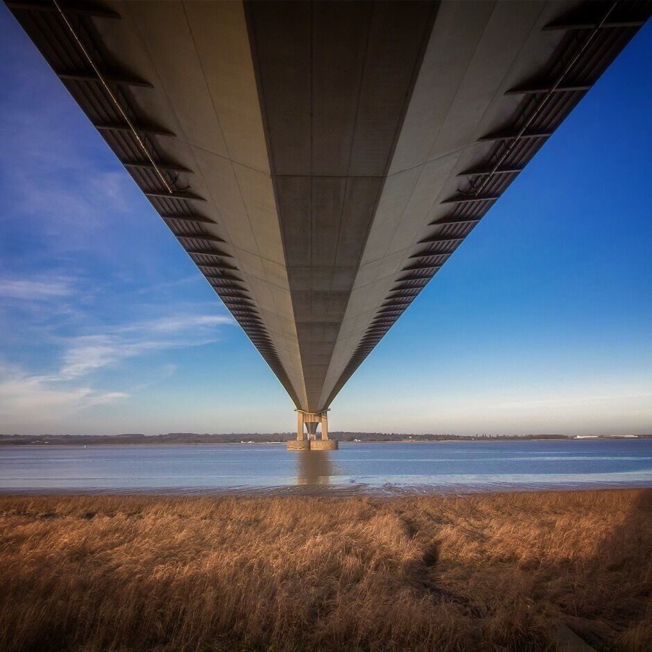 A bridge over a body of water with dry grass in the foreground.