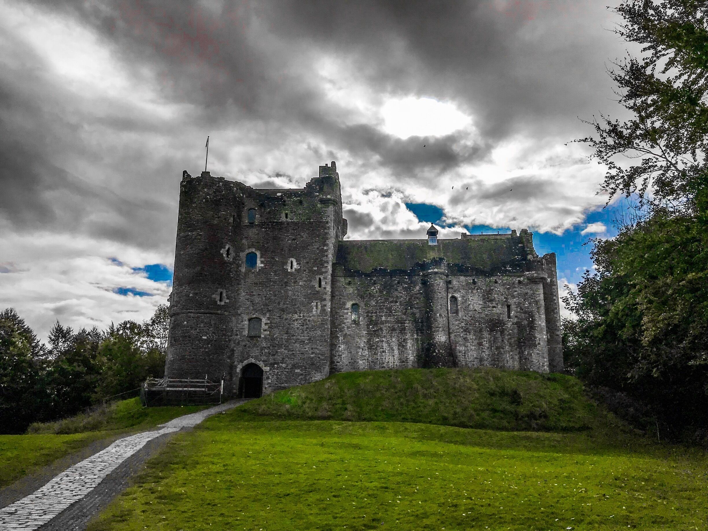 A historic castle with a tower, surrounded by green grass and trees.