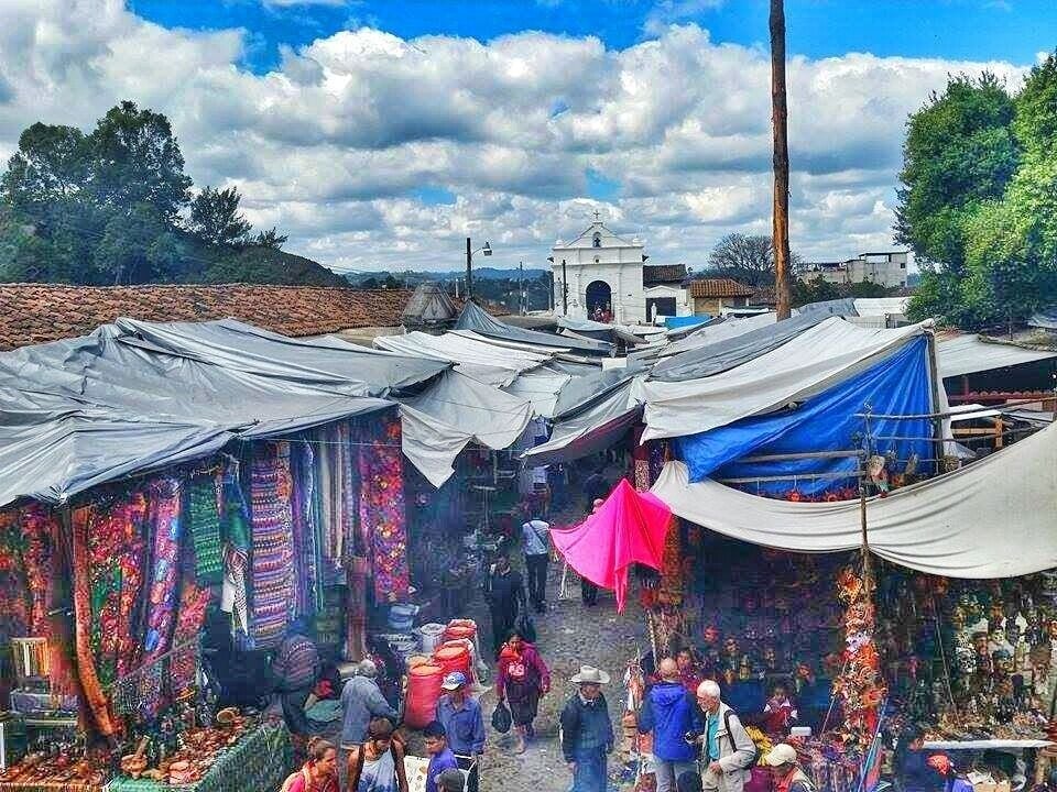 A bustling outdoor market with colorful stalls and a prominent white church in the background.
