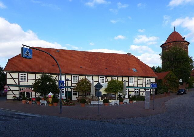 A traditional half-timbered building with a red-tiled roof, a tower, and outdoor seating.