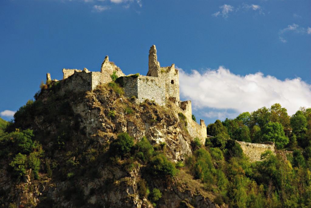 A historic stone castle on a hill with surrounding greenery.