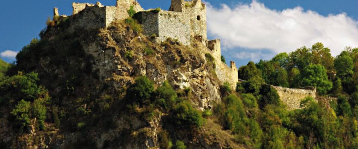 A historic stone castle on a hill with surrounding greenery.