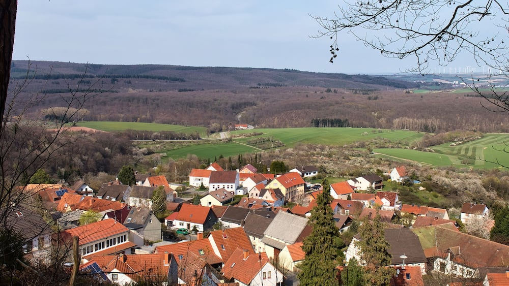 Sun shining on houses with red roofs in a small German village on a sunny spring day with fields and hills in the distance.