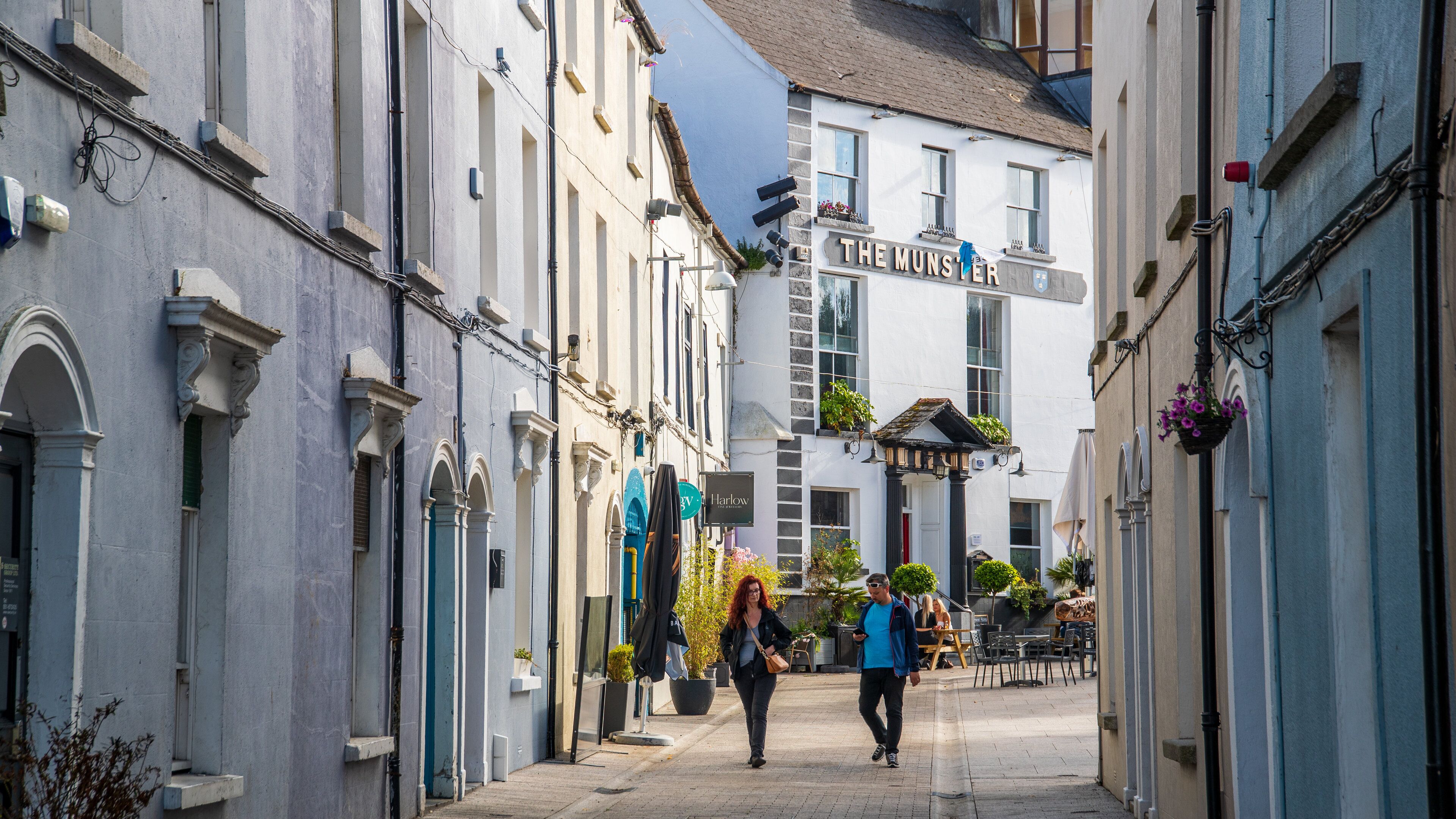 A narrow street with historic buildings, a sign for "The Munster," and outdoor seating areas.