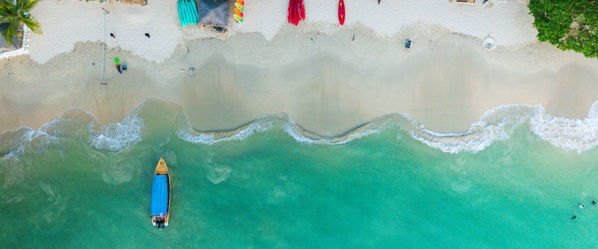 Una playa turquesa con un kayak y una pequeña embarcación.