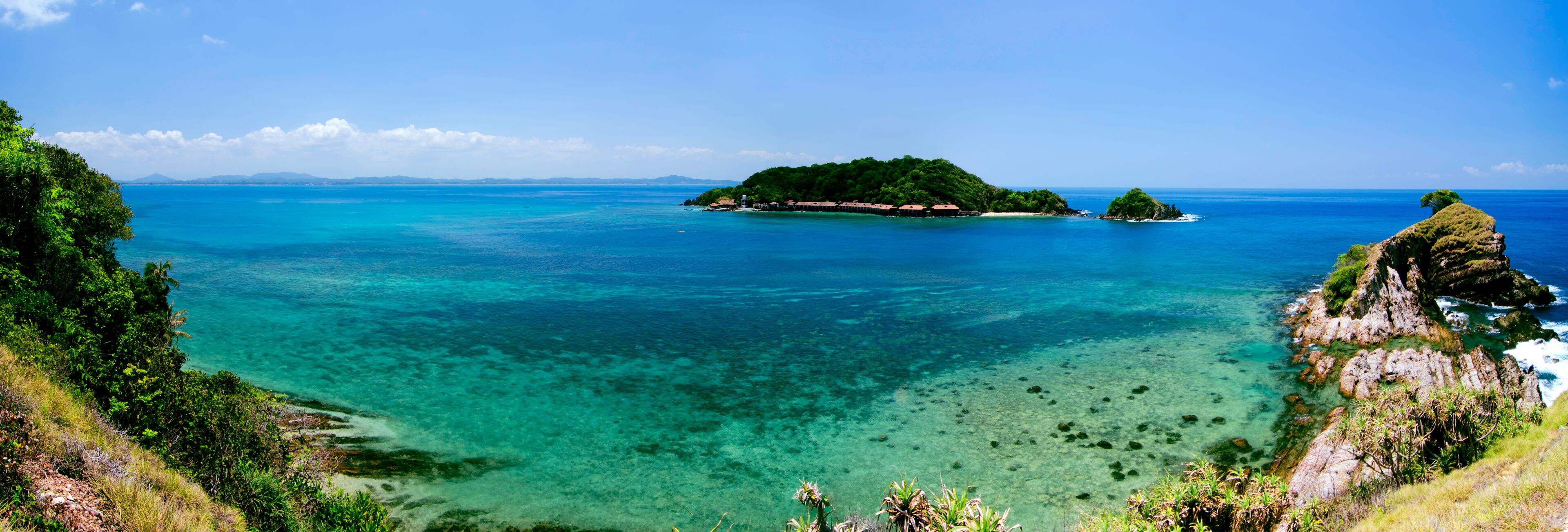 A tropical island surrounded by clear turquoise waters, lush greenery, and rocky coastlines.