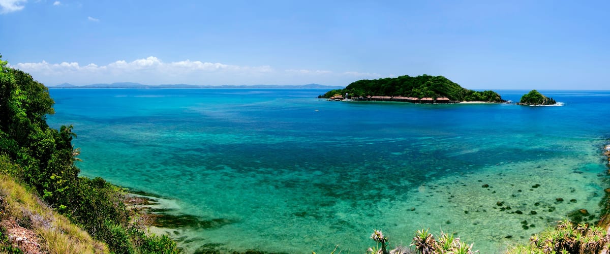 A tropical island surrounded by clear turquoise waters, lush greenery, and rocky coastlines.