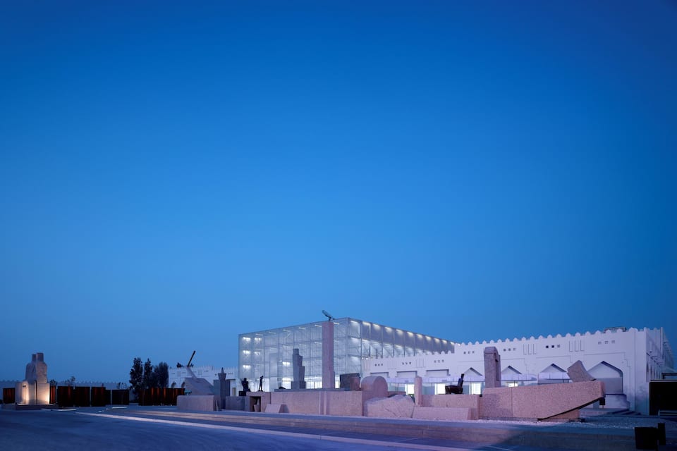 A modern building with a glass facade and a white exterior, surrounded by a landscaped area with large rocks and a clear sky.