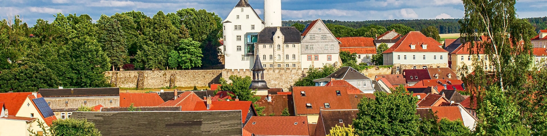 A historic town with a prominent white church, red-roofed houses, and lush greenery.