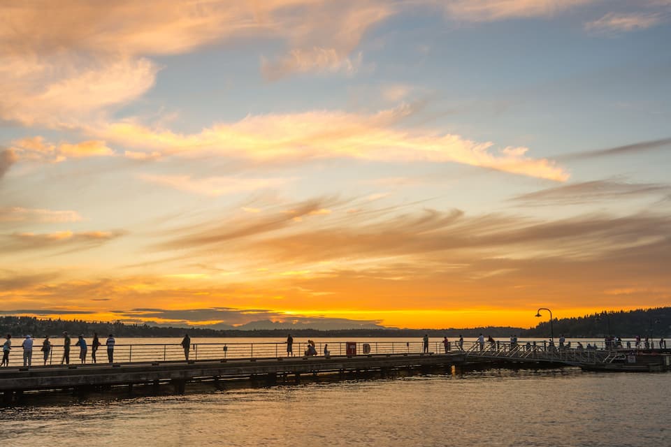A sunset over a body of water with a pier and people walking.
