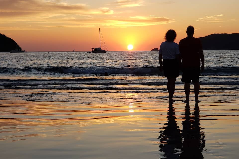 A sunset over a beach with two people standing and looking at the horizon.