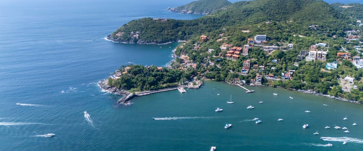 A coastal town with a marina, surrounded by hills and dense greenery.