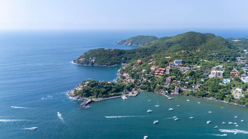 Un pueblo costero con un puerto deportivo, rodeado de colinas y abundante vegetación.