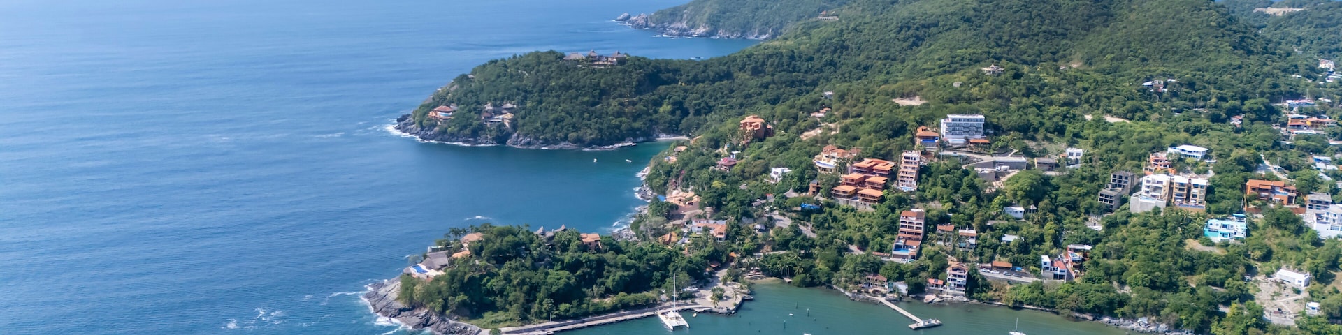 Une ville côtière dotée d’un port de plaisance, entourée de collines et d’une végétation luxuriante.