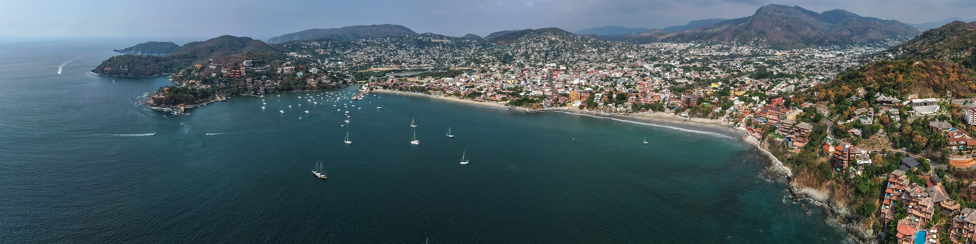 A coastal city with a bay, numerous sailboats, and a mountainous backdrop.