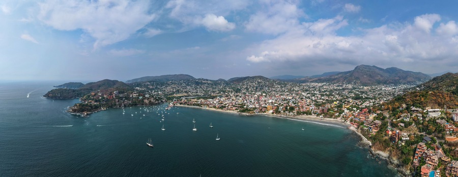 Una ciudad costera con una bahía, numerosos veleros y montañas al fondo.