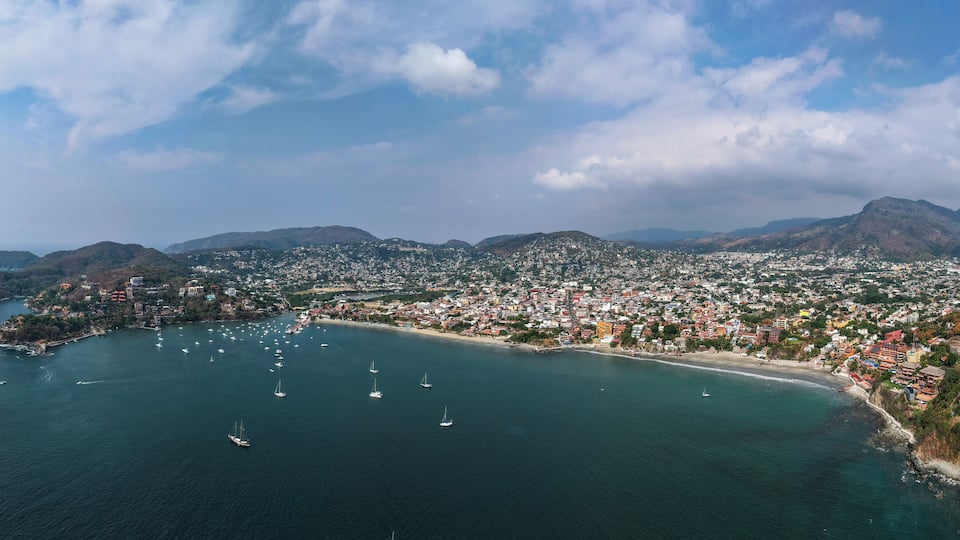 A coastal city with a bay, numerous sailboats, and a mountainous backdrop.