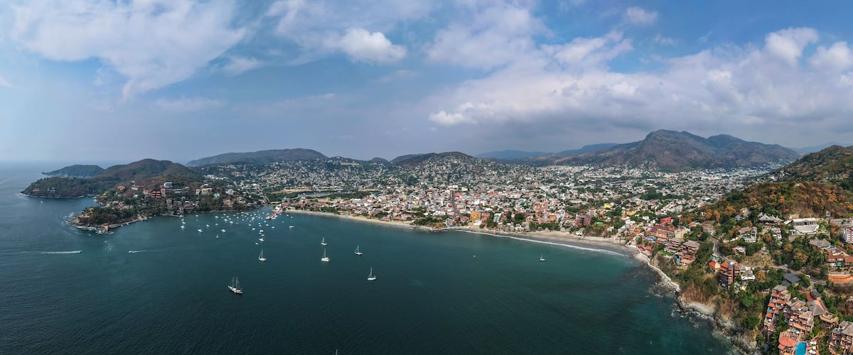 A coastal city with a bay, numerous sailboats, and a mountainous backdrop.