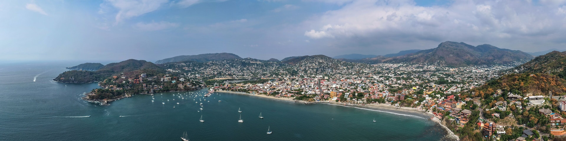 A coastal city with a bay, numerous sailboats, and a mountainous backdrop.