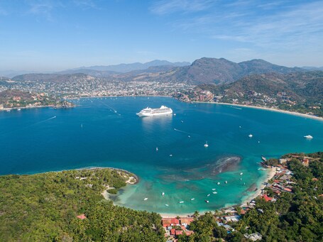 Eine Küstenstadt mit einem großen Kreuzfahrtschiff, klarem, blauem Wasser und umliegenden Bergen.
