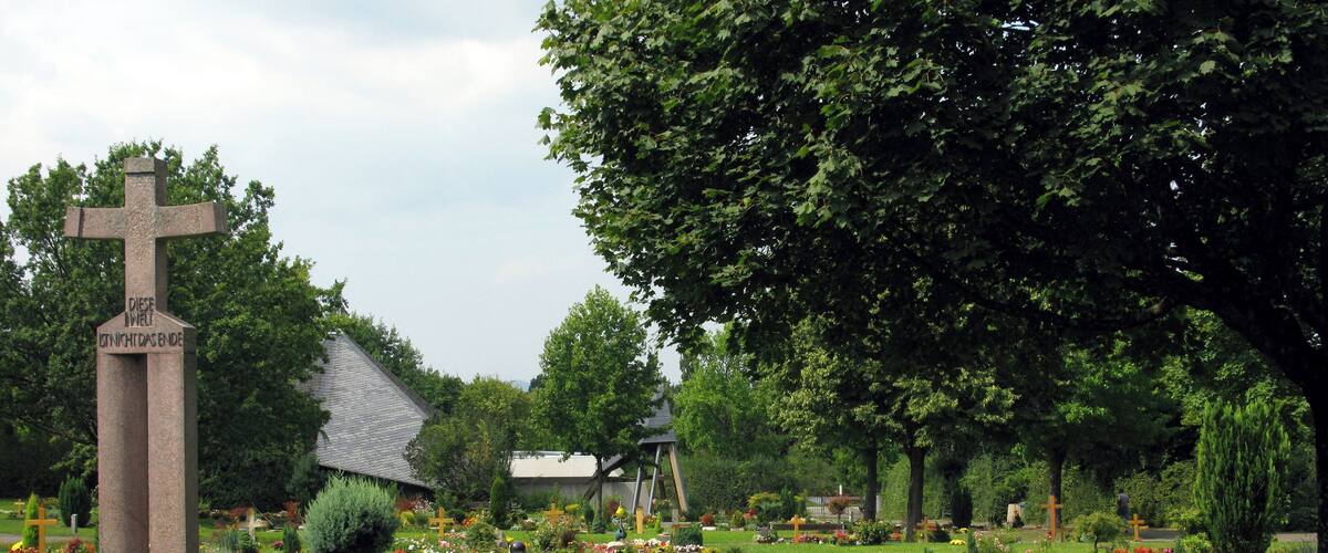 A cemetery with a large cross monument, surrounded by trees and colorful flowers.