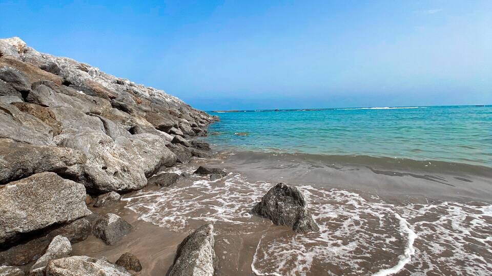 A rocky coastline with waves crashing onto the shore under a clear blue sky.