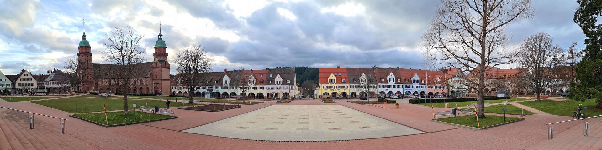 A large open square with a central plaza, surrounded by historic buildings with red roofs and a prominent tower.