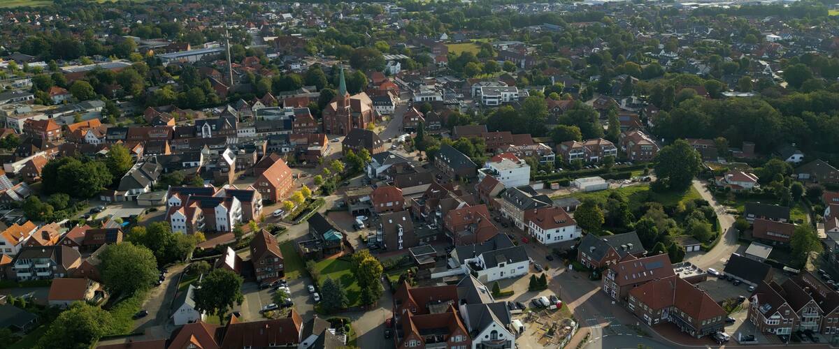 An aerial view of a town with wind turbines in the distance, surrounded by residential buildings and greenery.