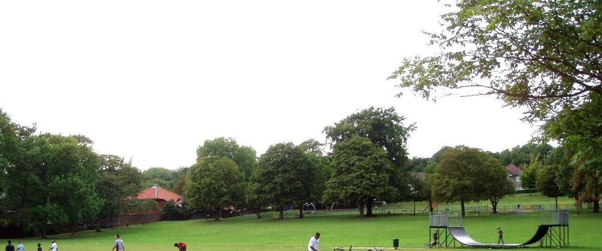 A park with a grassy field, a playground, and a walking path.