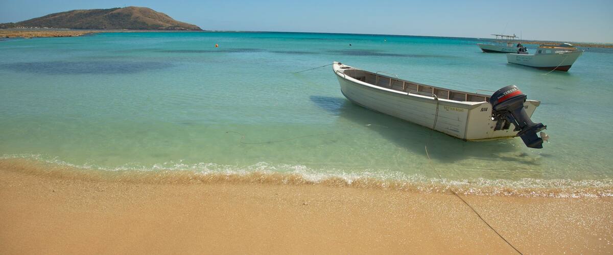 A beach with clear turquoise water, a sandy shore, and two boats anchored near the water's edge.