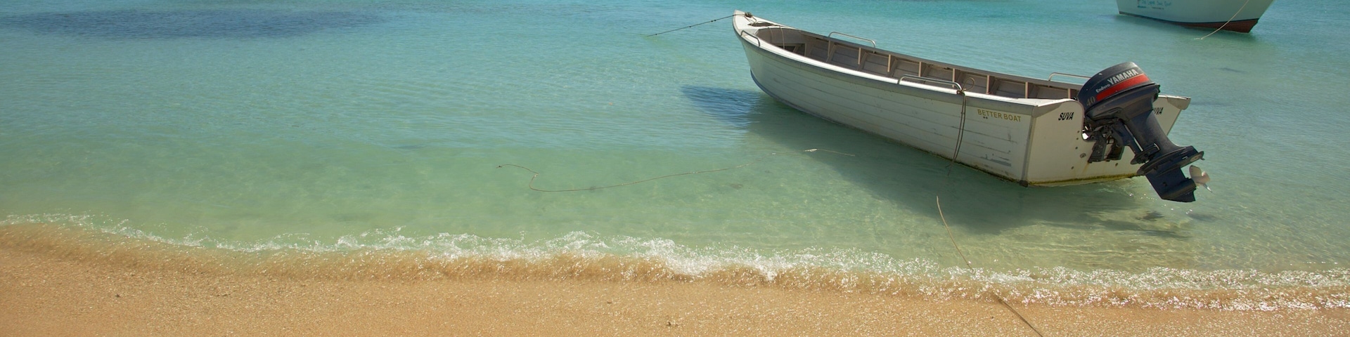 A beach with clear turquoise water, a sandy shore, and two boats anchored near the water's edge.