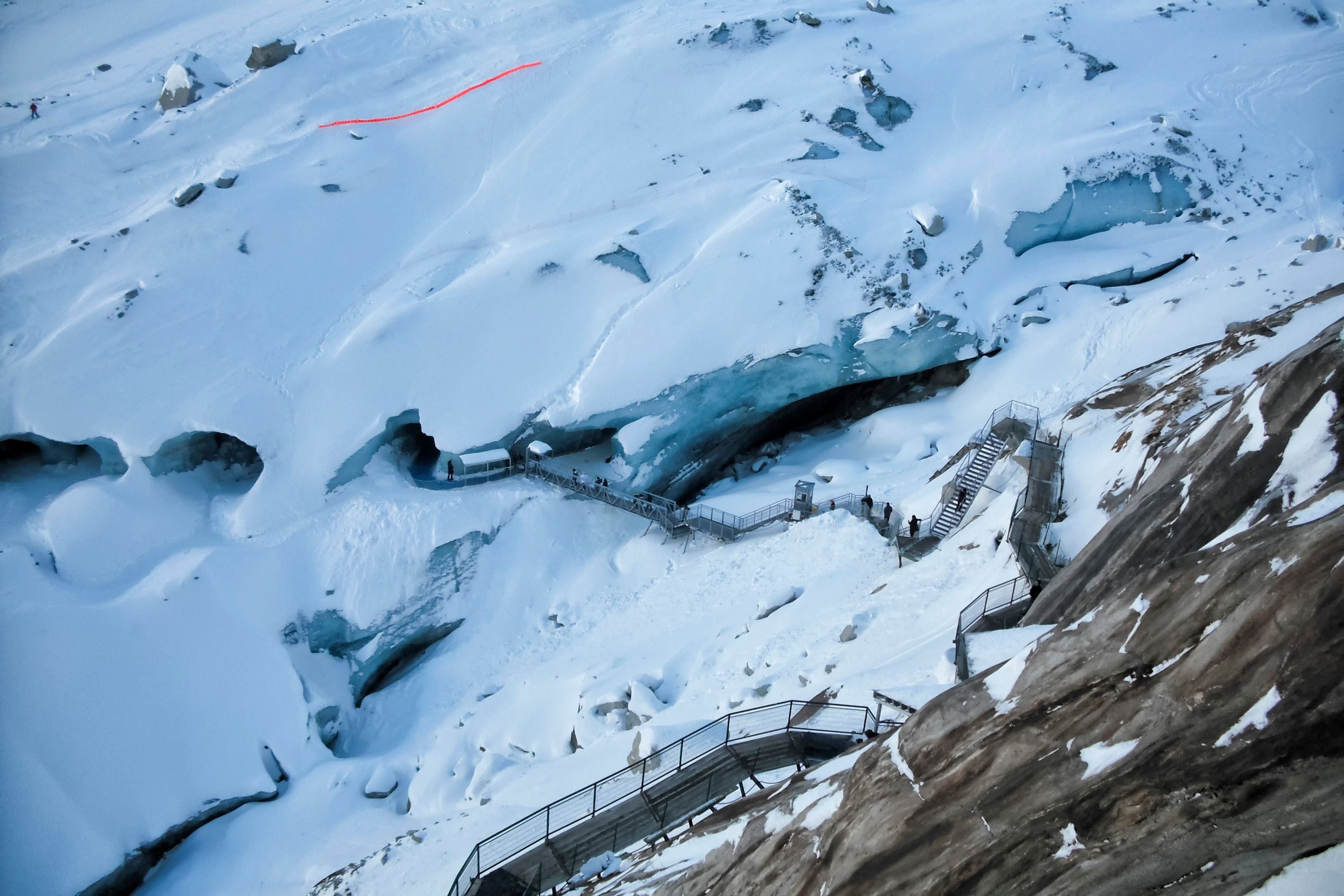 A snow-covered mountain with a glacier, a red line marking a path, and a staircase leading down.