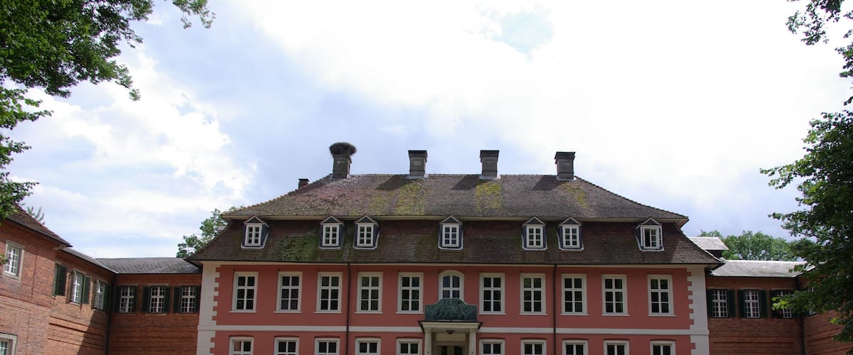 A large red brick building with a symmetrical facade, a central entrance, and a well-manicured garden with a fountain.