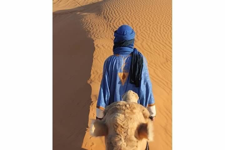A person riding a camel in a desert with sand dunes.