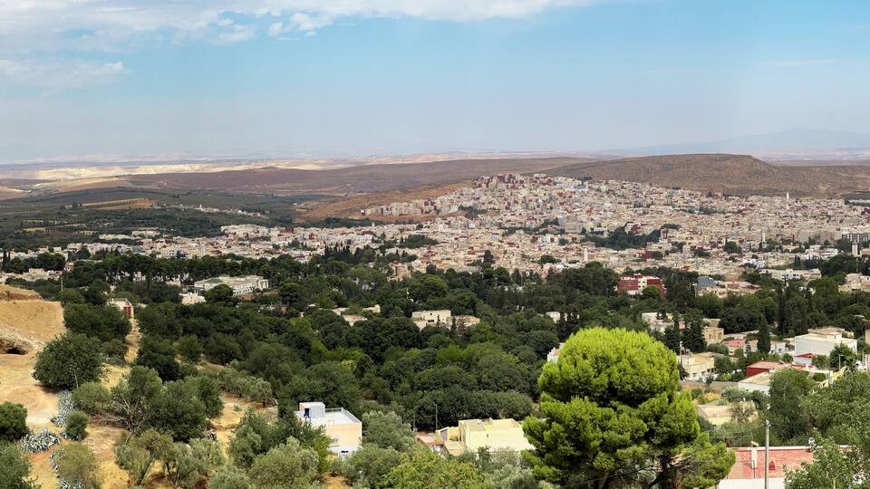 A cityscape with a dense urban area surrounded by hills and sparse vegetation.