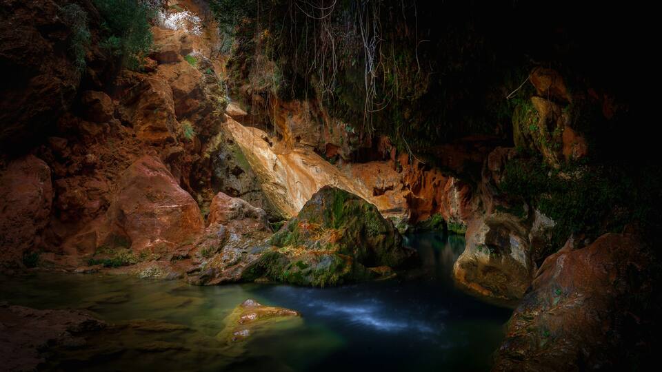 A cave with a flowing stream and moss-covered rocks.