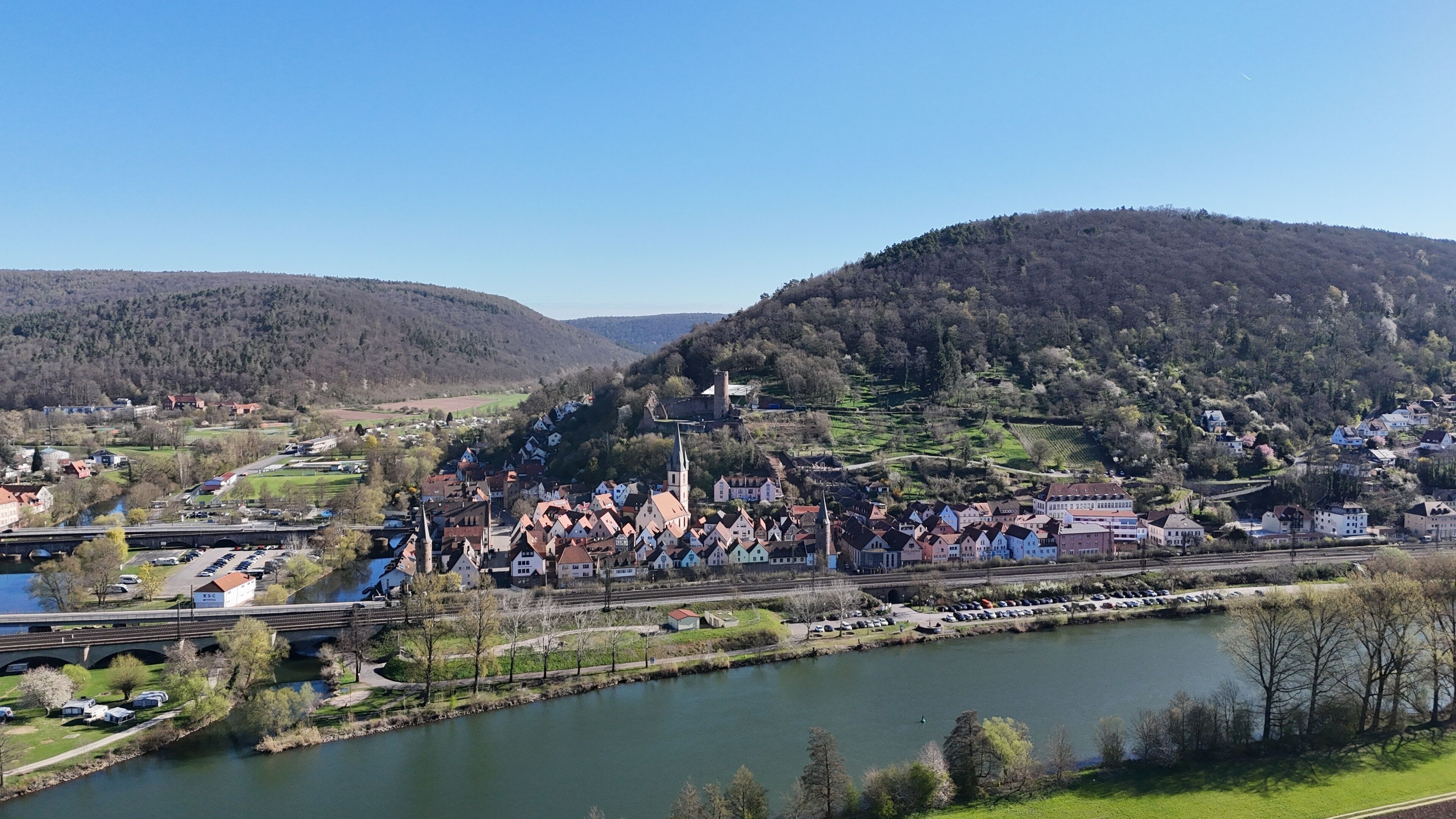 A riverside town with historic buildings, a bridge, and a hill with a church.