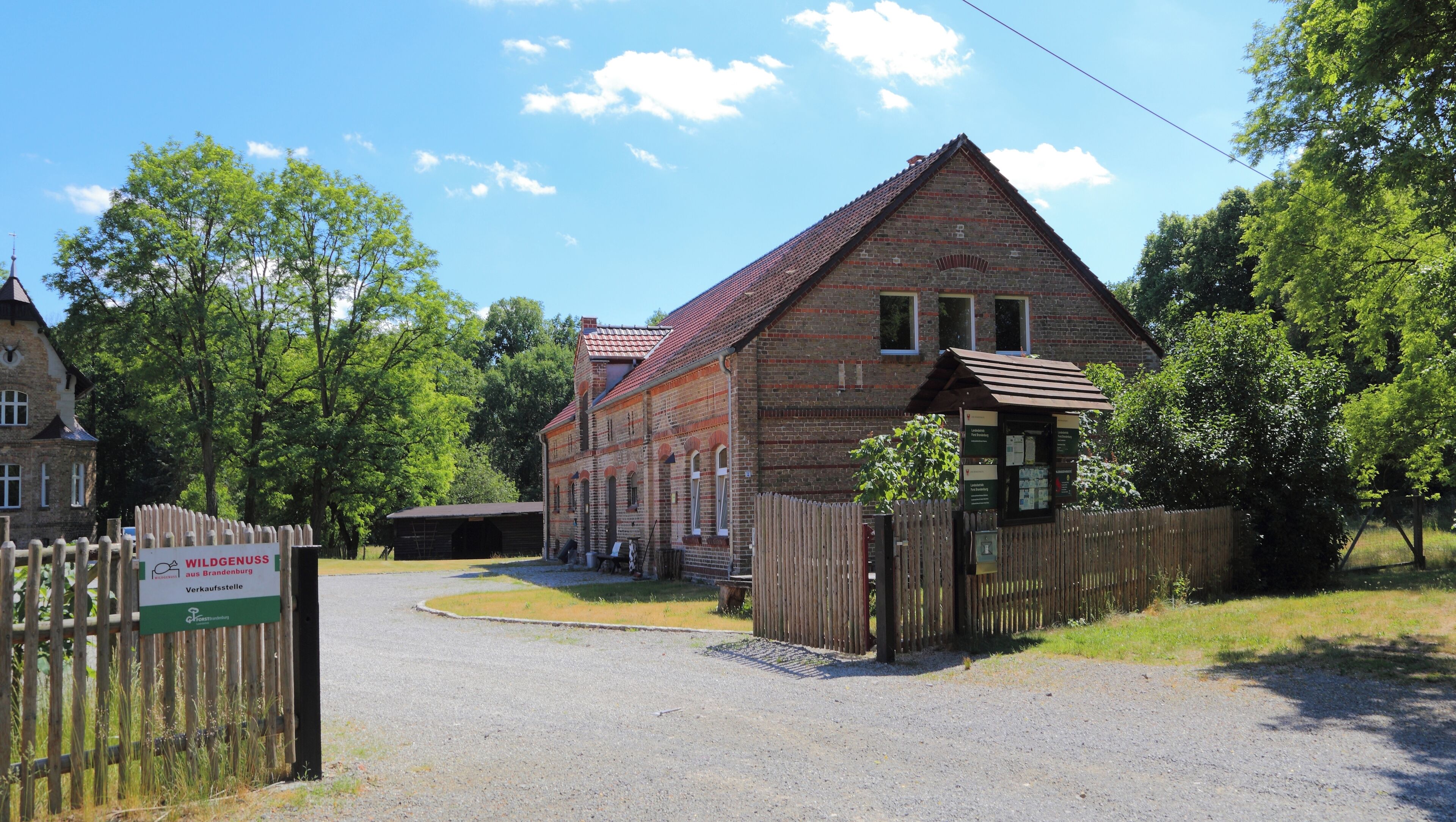 A brick building with a red roof, surrounded by trees and a wooden fence.