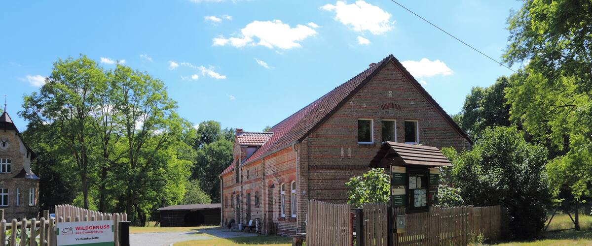 A brick building with a red roof, surrounded by trees and a wooden fence.
