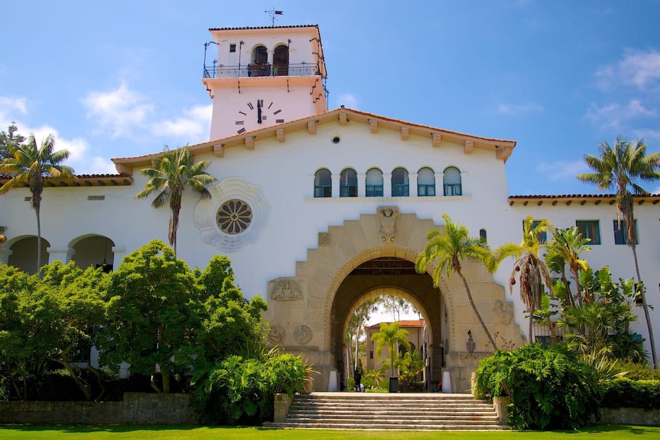 Um edifício histórico com torre de relógio, janelas em arco e um arco central.